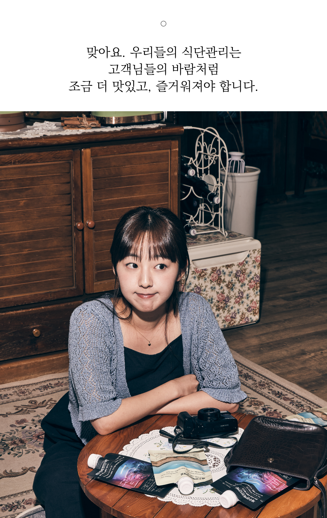 실내에서 카메라와 책을 앞에 두고 앉아있는 여성 : 맞아요. 우리들의 식단관리는 고객님들의 바람처럼 조금 더 맛있고, 즐거워져야 합니다.
